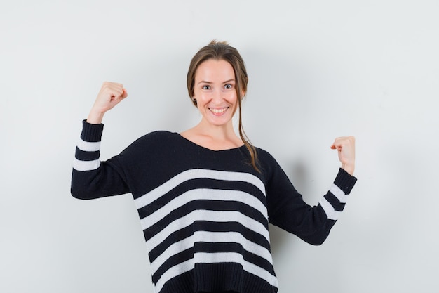 Gratis foto de jonge vrouw die winnaar toont stelt in zwarte blouse en zwarte broek en kijkt gelukkig