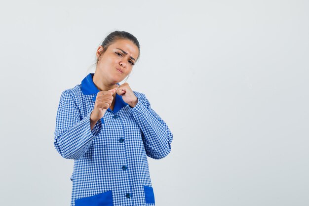 De jonge vrouw die zich in bokser bevindt stelt in het blauwe overhemd van de gingangpyjama en kijkt mooi, vooraanzicht.