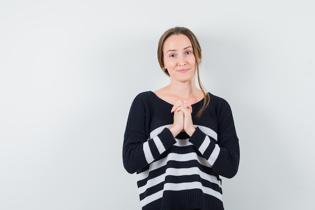 De jonge vrouw die zich in gebed bevindt stelt in zwarte blouse en zwarte broek en kijkt optimistisch