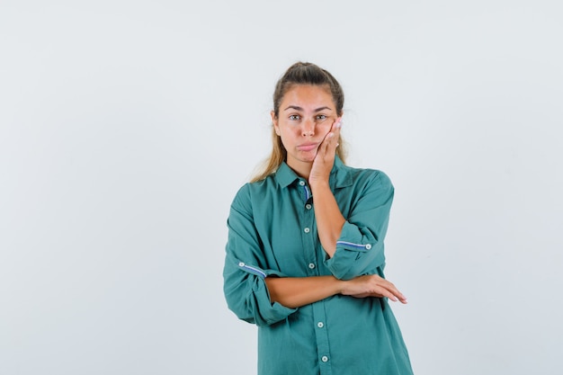 De jonge vrouw die zich in het denken bevindt stelt in groene blouse en peinzend kijkt