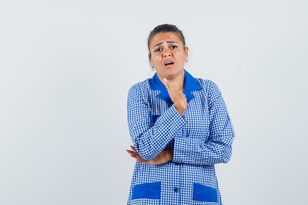 De jonge vrouw die zich in het denken stelt, balde vuist in het blauwe overhemd van de gingangpyjama en gestrest kijkt. vooraanzicht.