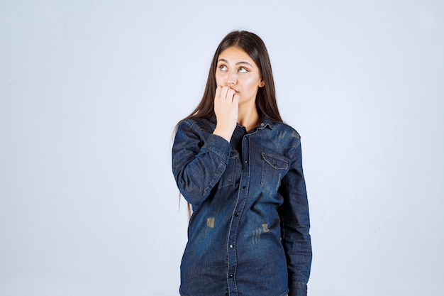 De jonge vrouw in spijkeroverhemd kijkt verward en bedachtzaam