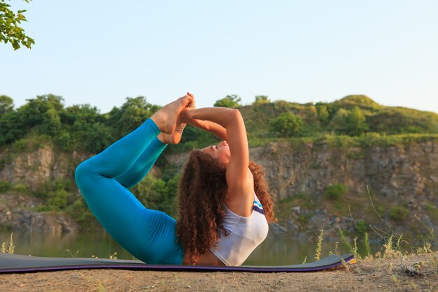 De jonge vrouw oefent yoga dichtbij rivier uit