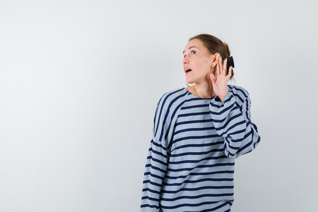 De jonge vrouw probeert te horen door haar hand achter haar oor op een witte achtergrond te plaatsen