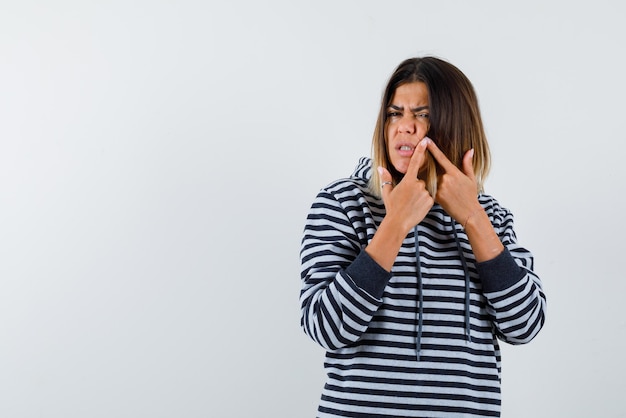 De jonge vrouw toont iets op de wang met wijsvingers op een witte achtergrond