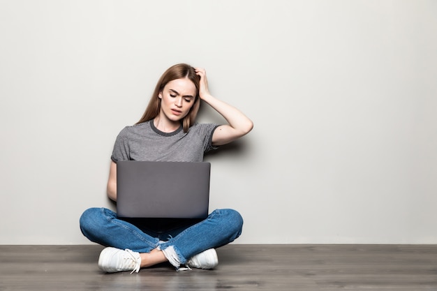 De jonge vrouwenzitting op haar huisvloer vermoeide en zeer slaperig houdend hand op hoofd dat op grijze muur wordt geïsoleerd