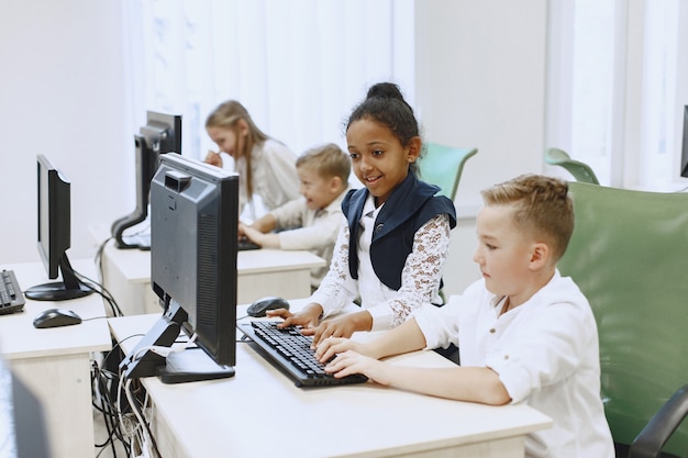 De jongen en het meisje zitten aan tafel. Afrikaans meisje in de klas van de informatica. Kinderen spelen van computerspelletjes.