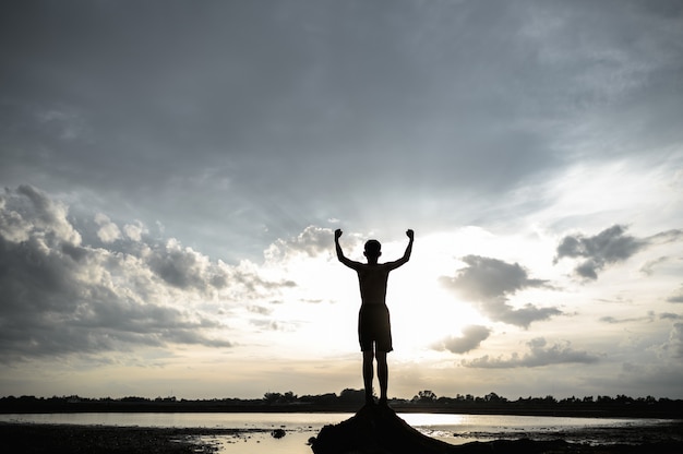 Gratis foto de jongen stak zijn hand op in de lucht om regen te vragen tijdens de zonsondergang.