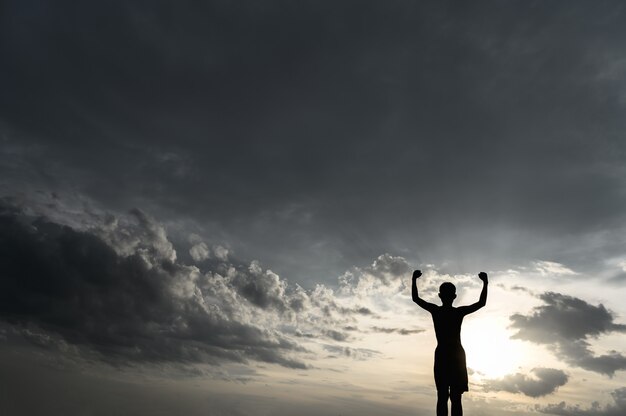 De jongen stak zijn hand op in de lucht om regen te vragen tijdens de zonsondergang.