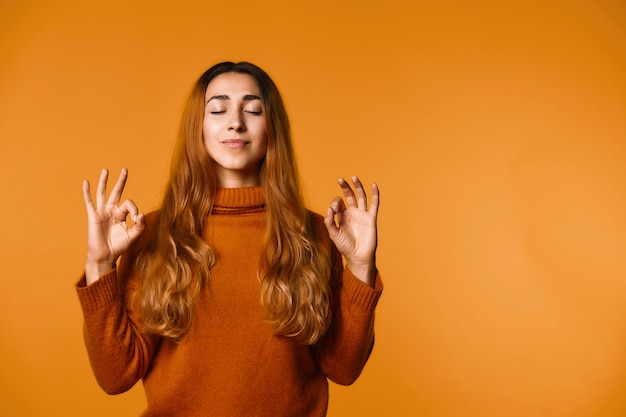 Gratis foto de kalme roodharige kaukasische vrouw gekleed in sweater, met gesloten ogen, concentreert zich en ontspant