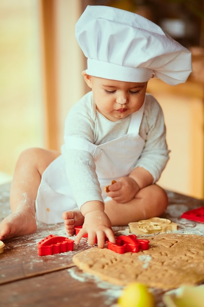 De kleine baby zit op de tafel in de buurt van deeg