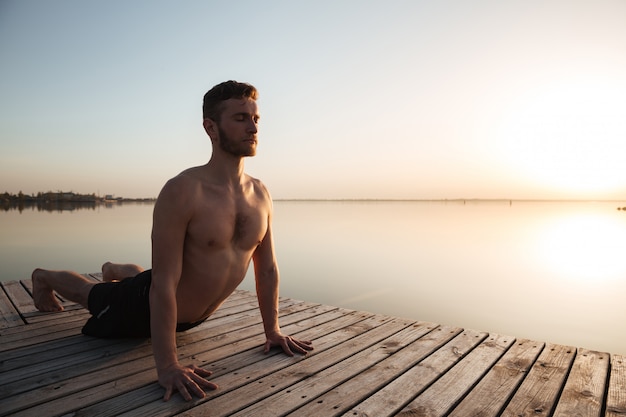 De knappe jonge sportman maakt yogaoefeningen bij het strand.