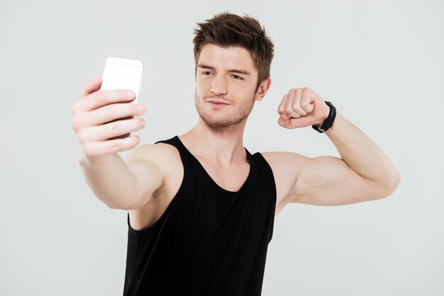 De knappe jonge sportman met telefoon maakt selfie