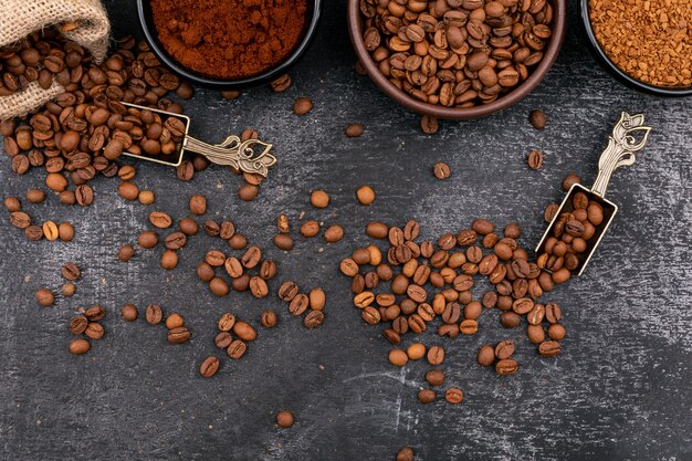 de koffiebonen in kommen metalen lepel en zak op een donkere ondergrond