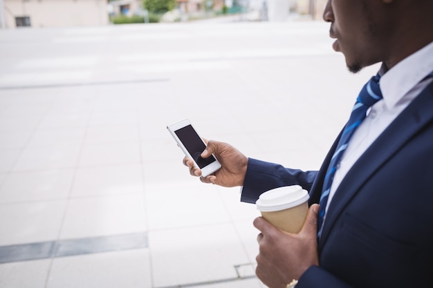 De koffiekop van de zakenmanholding en het gebruiken van mobiele telefoon