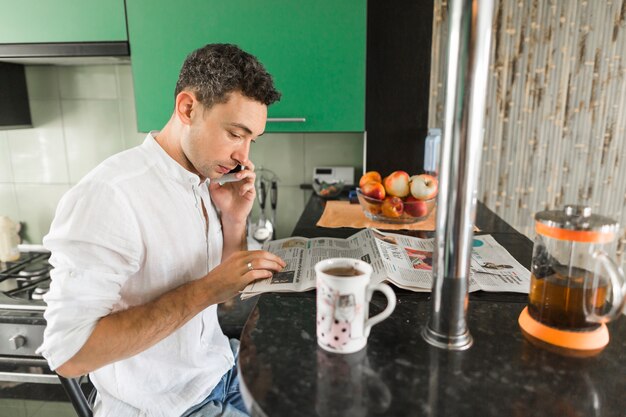 De krant die van de jonge mensenlezing op mobiele telefoon bij keukenteller spreekt