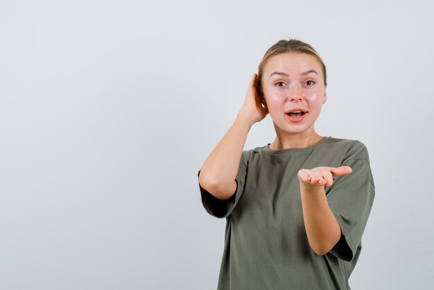 De lachende blonde vrouw toont camera met haar hand op witte achtergrond