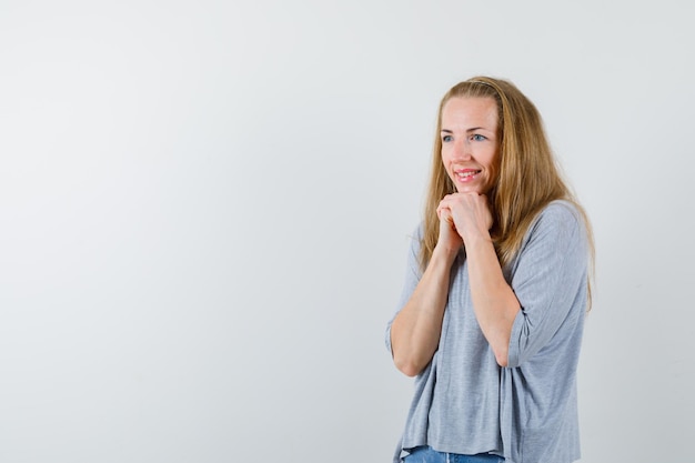 De lachende jonge vrouw kijkt naar beneden door handen bij elkaar te houden onder de kin op een witte achtergrond
