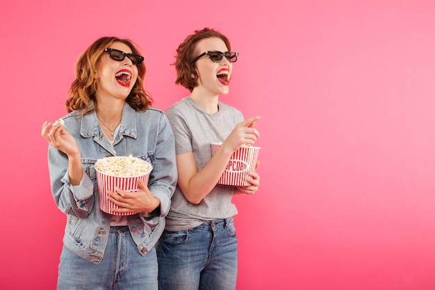 De lachende vrouwenvrienden die popcorn eten letten op film.