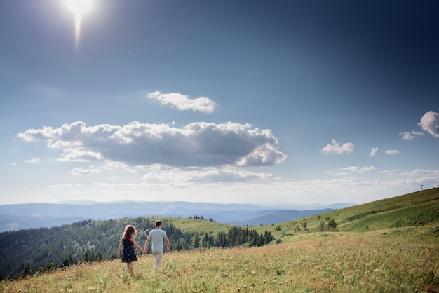 De man en de vrouw houden hun handen samen lopend op de heuvel ergens in de bergen