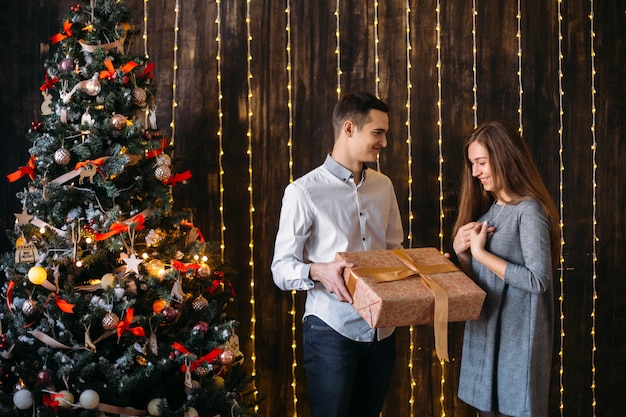 De man geeft een cadeau aan de vrouw die voor een kerstboom staat