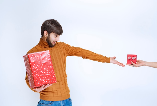 Gratis foto de man heeft een grote rode geschenkdoos en verlangt ernaar om nog een kleine te nemen.