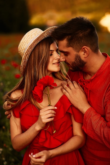 De man houdt tedere mooie vrouw die zich met haar op het groene gebied met rode papavers bevindt