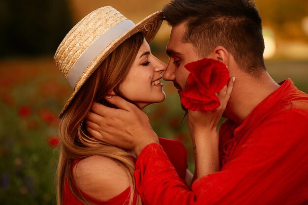 De man houdt tedere mooie vrouw die zich met haar op het groene gebied met rode papavers bevindt