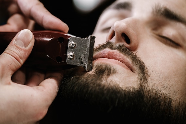 De man sluit zijn ogen terwijl de kapper zijn zwarte baard vormt