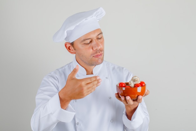 De mannelijke tomaten en de paddestoelen van de chef-kokholding in kom in hoed en uniform