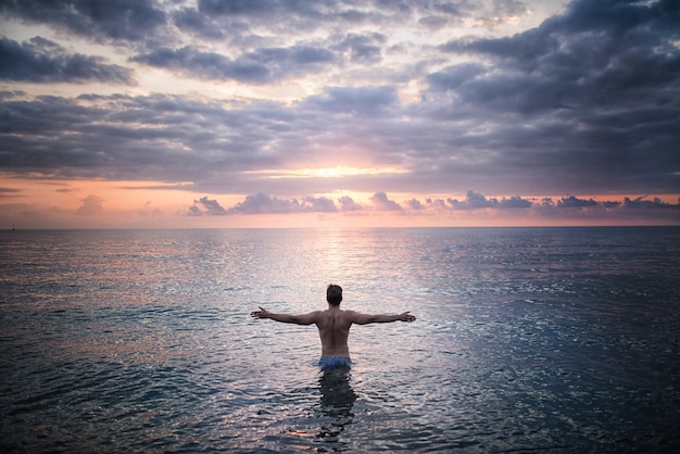 De mens bevindt zich in het zeewater die zonsondergang onder ogen zien