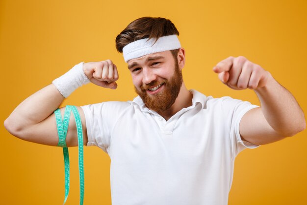 De mens die van sporten zijn bicepsen meet en vinger op camera richt