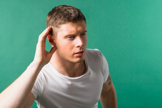 Gratis foto de mens houdt haar hand dichtbij oor en luistert zorgvuldig tegen groene achtergrond