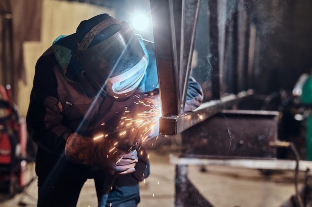 De mens werkt in een metaalfabriek, hij last een stuk spoorstaaf met speciaal gereedschap.