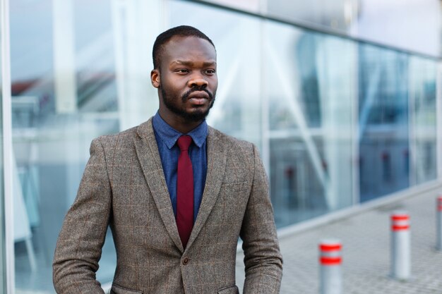 De modieuze Afrikaanse Amerikaanse zwarte zakenman stelt in een kostuum vóór een modern gebouw