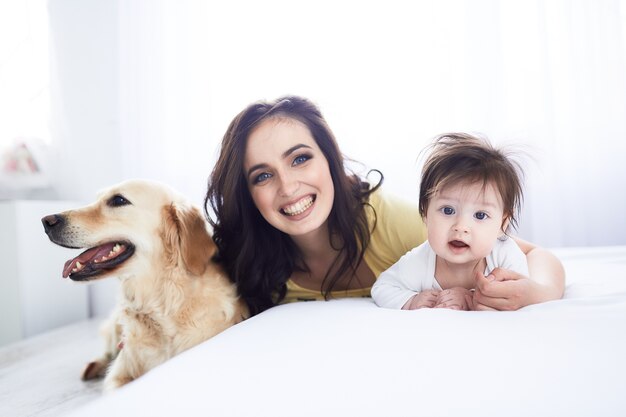 De moeder met dochter ligt op het bed en de hond zit in de buurt van bed