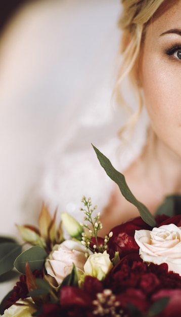 Gratis foto de mooie blondebruid kijkt over donkerrood huwelijksboeket