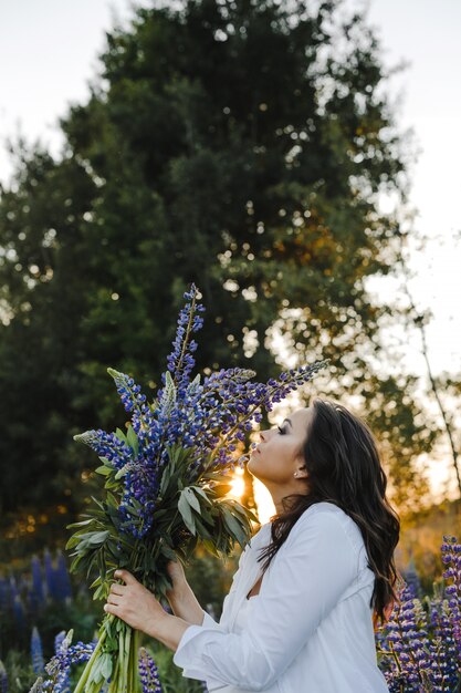 De mooie dame ruikt een boeket van lupines op zonsondergang