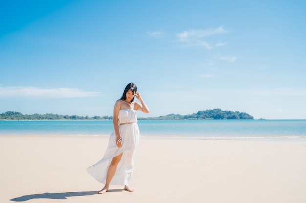 De mooie jonge Aziatische gelukkige vrouw ontspant lopend op strand dichtbij overzees.