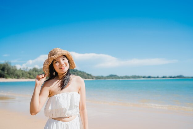 De mooie jonge Aziatische gelukkige vrouw ontspant lopend op strand dichtbij overzees.