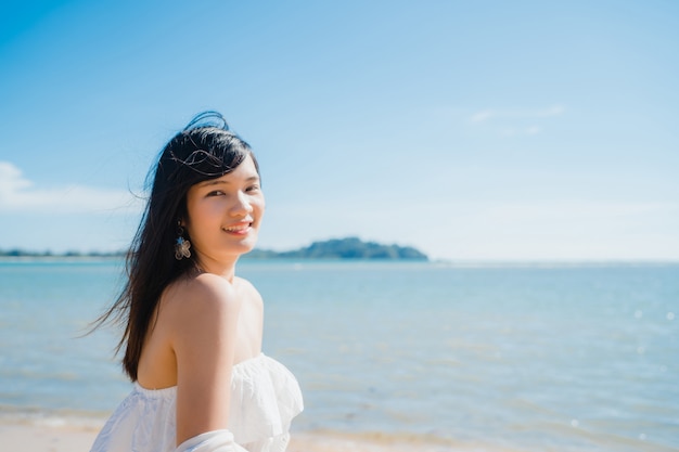 De mooie jonge Aziatische gelukkige vrouw ontspant lopend op strand dichtbij overzees.