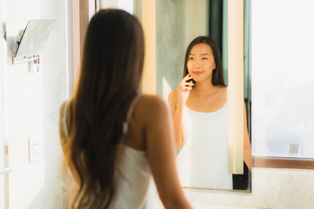 De mooie jonge Aziatische vrouw controleert haar gezicht in badkamers