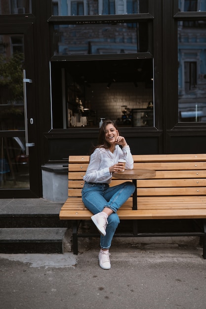 Gratis foto de mooie jonge vrouw in straatkoffie drinkt koffie