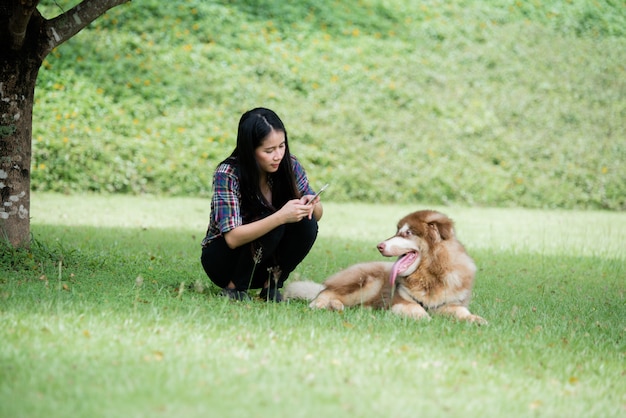 De mooie jonge vrouw vangt in openlucht foto met haar kleine hond in een park. Levensstijl portret.