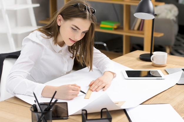 De mooie jonge vrouwelijke schets van de architectentekening op Witboek over het houten bureau