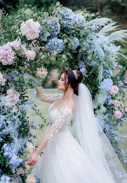 De mooie Kaukasische donkerbruine bruid bevindt zich dichtbij de overwelfde galerij in openlucht van blauwe en roze hydrangea hortensia wordt gemaakt die