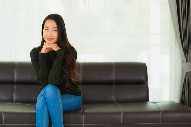 De mooie portret jonge Aziatische vrouw zit ontspant op bank