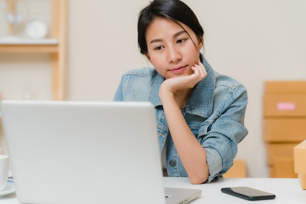 De mooie slimme Aziatische jonge ondernemer van de ondernemers bedrijfsvrouw van online het controleren van het MKB product op voorraad en sparen aan computer die thuis werken.