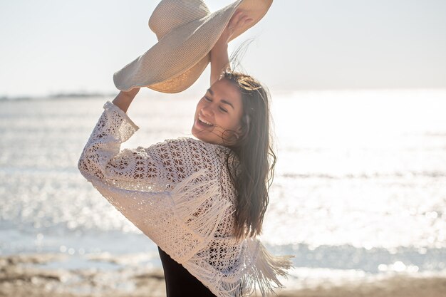 De mooie vrouw glimlacht en houdt een hoed in haar handen. Zee vakantie concept.