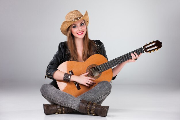 De mooie vrouw in een cowboyhoed en akoestische gitaar.